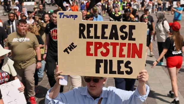 A crowd of people, one in the foreground holds a sign that reads: Release the Epstein files