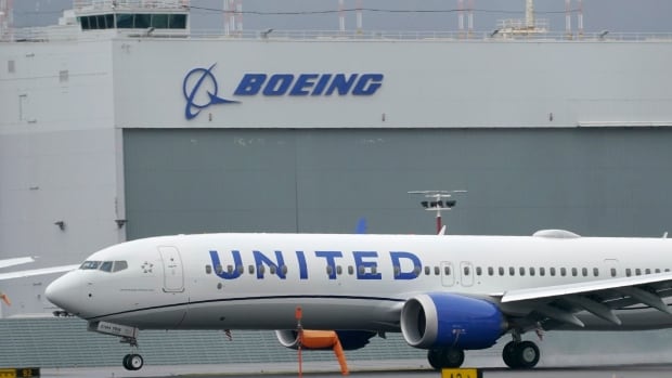 A plane that has the logo United on its side is shown on the tarmac, in front of a building that has a Boeing logo.