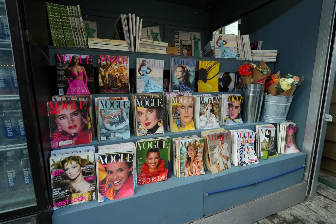 A newsstand with various issues of Vogue magazines on the shelves.