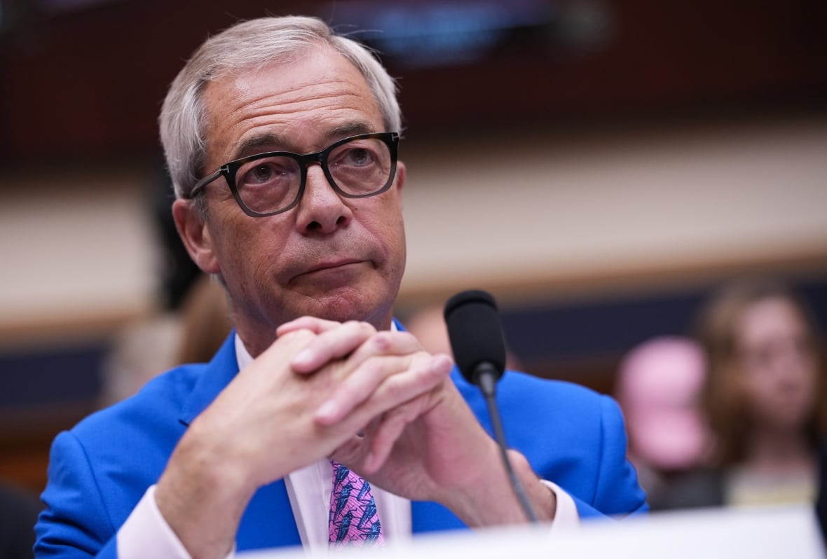 A clean man with glasses wearing a bright blue suit sit near the microphone.