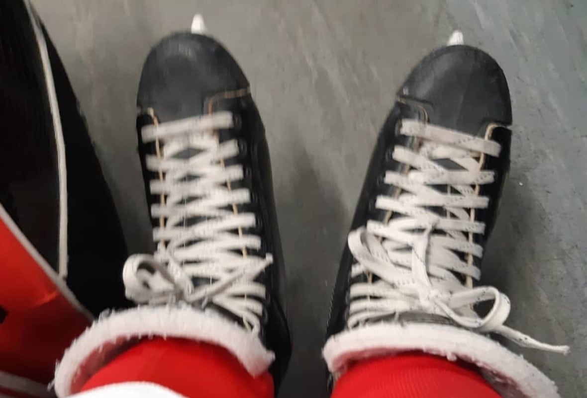 Zwei Beine in roten Hockeyhosen und ein Paar schwarze Hockeyschlittschuhe an den Füßen der Person.