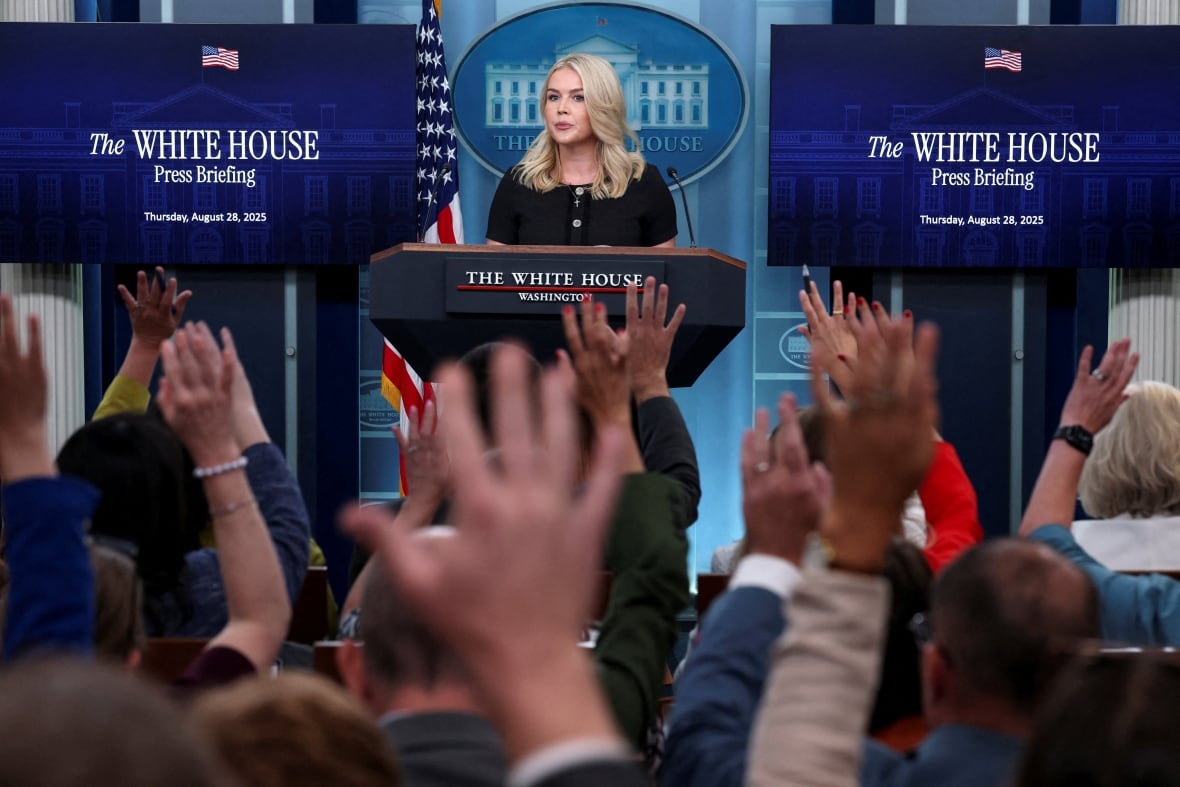 A woman stands in a lecture at the White House while journalists raised their hands to ask questions.