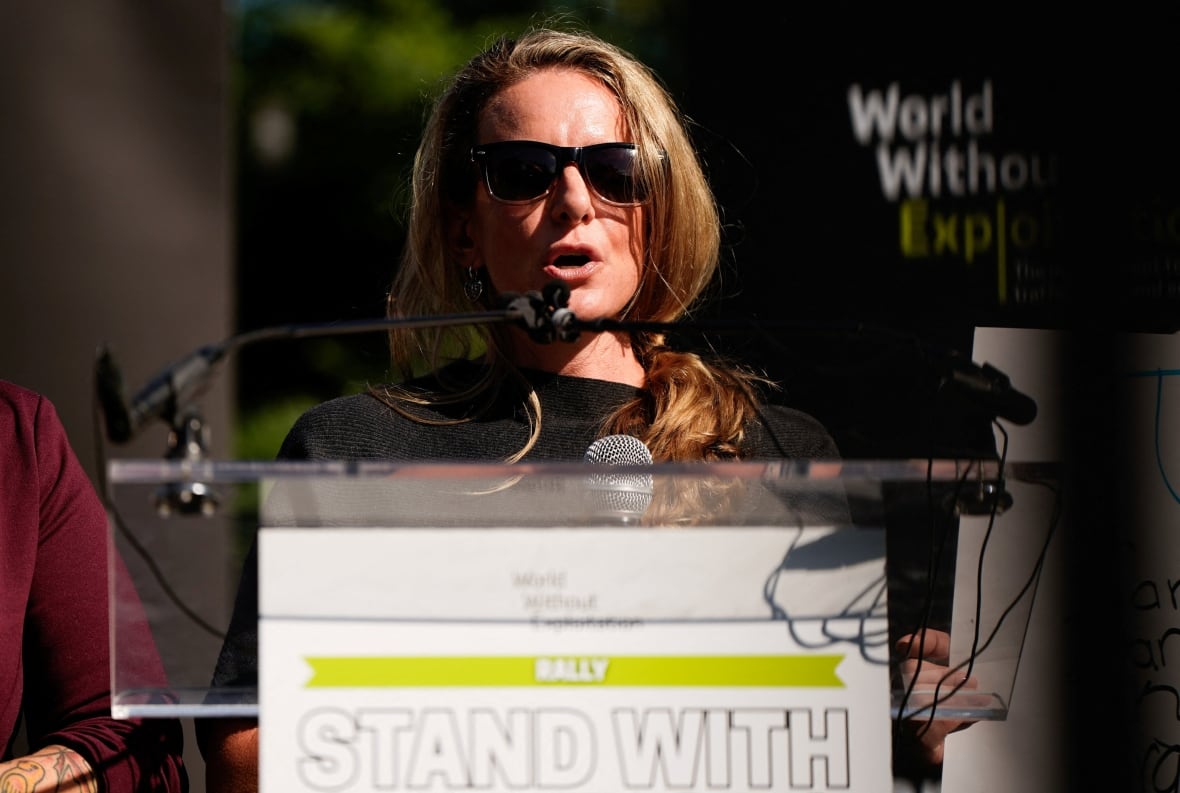 A woman with long hair and sunglasses speak on the outer platform