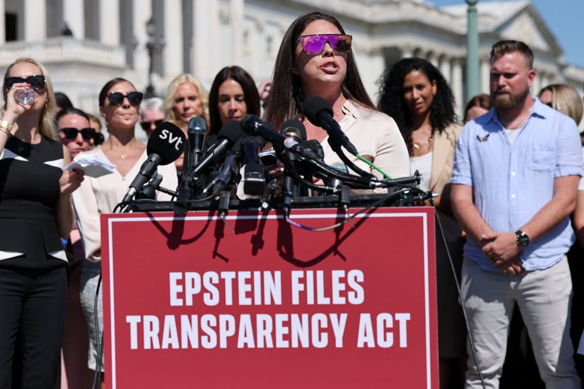 A white woman speaks with sunglasses on a platform bearing a sign that says Epsin's transparent law.