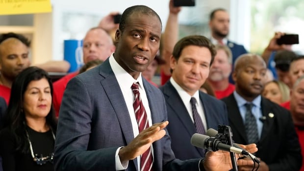 FILE - Florida Surgeon General Dr. Joseph Ladapo gestures as speaks to supporters and members of the media before a bill signing by Gov. Ron DeSantis, Nov. 18, 2021, in Brandon, Fla. A man in a suit stands at a podium, speaking into a microphone and gesturing with his hands.