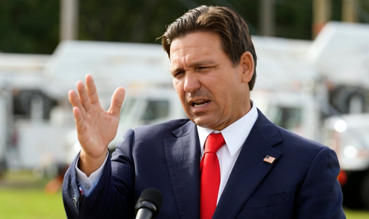 A man wearing a suit urges while speaking to a microphone with one hand raised in a gesture.