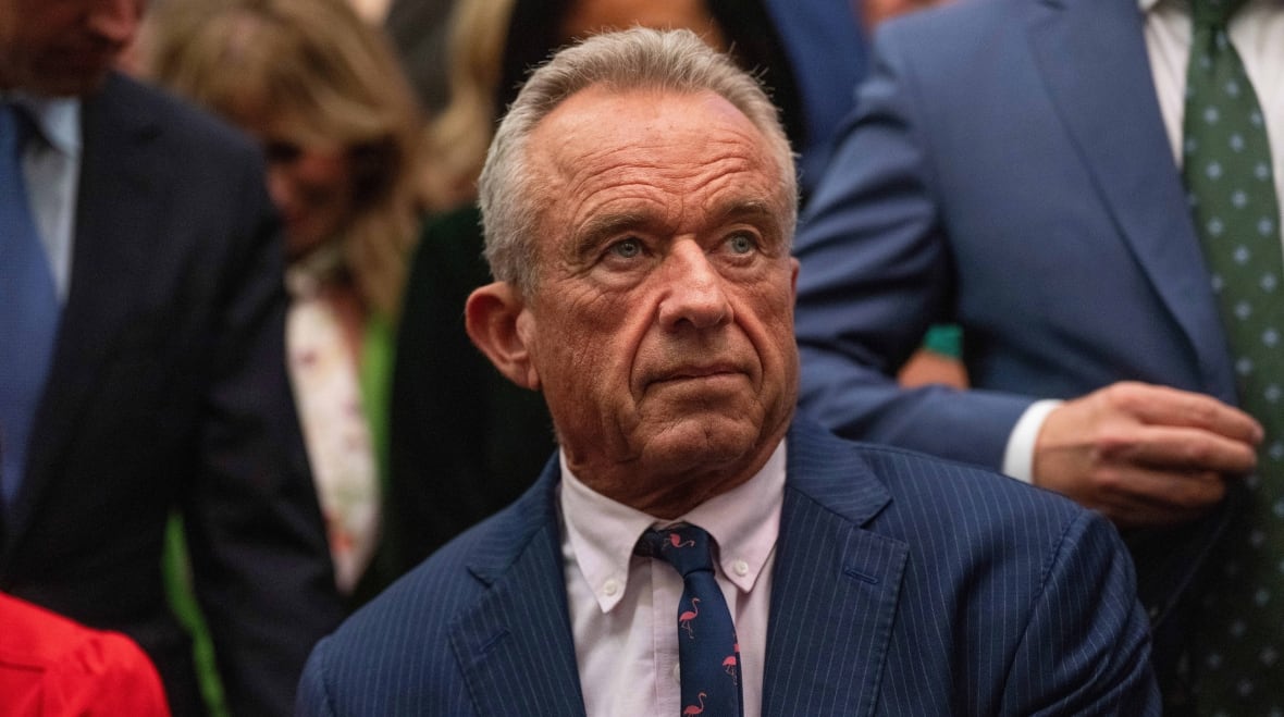 A man was seen wearing a suit sitting with another standing around him.