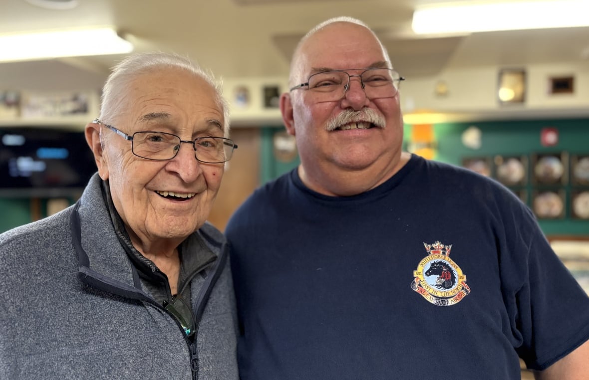 Two men stand smiling.