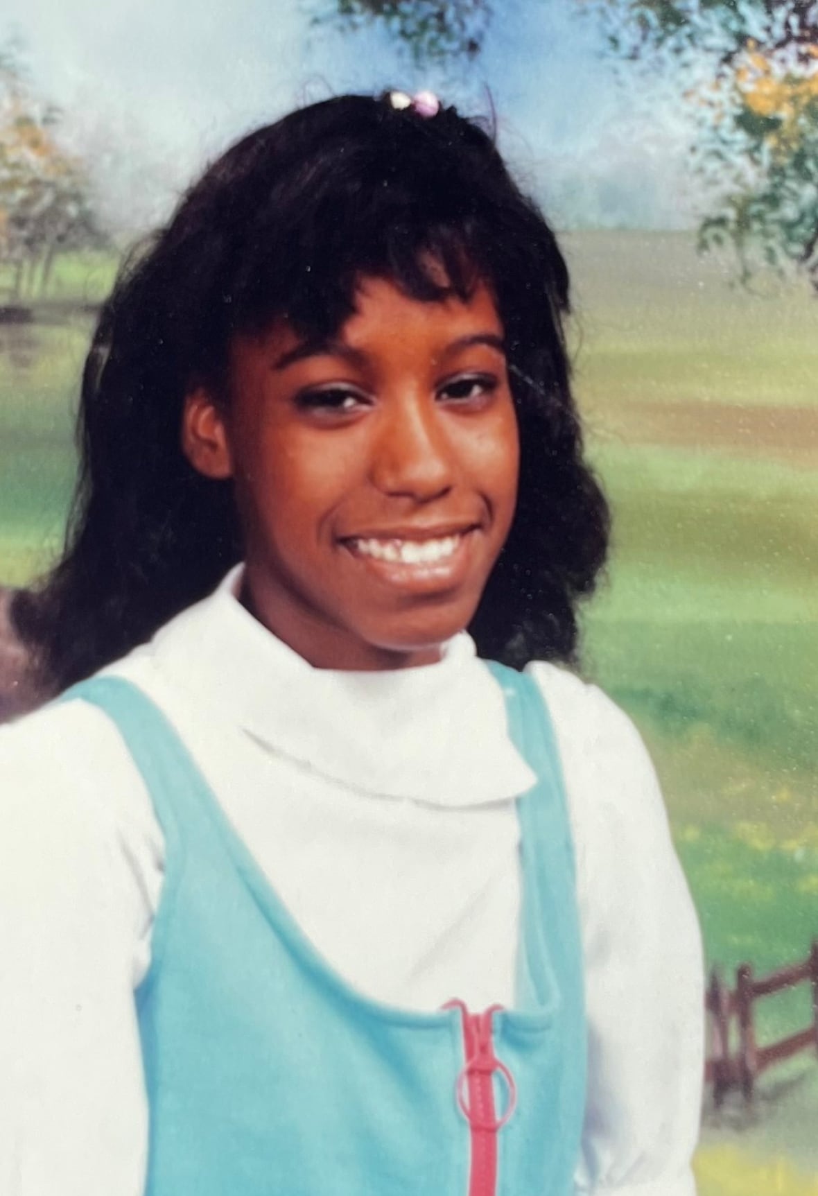 A Black girl with hair bangs and wearing a blue and white dress smiles for a portrait.