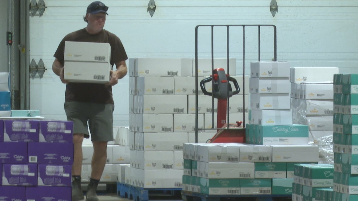 A man carries a crate of beer cans in a warehouse.