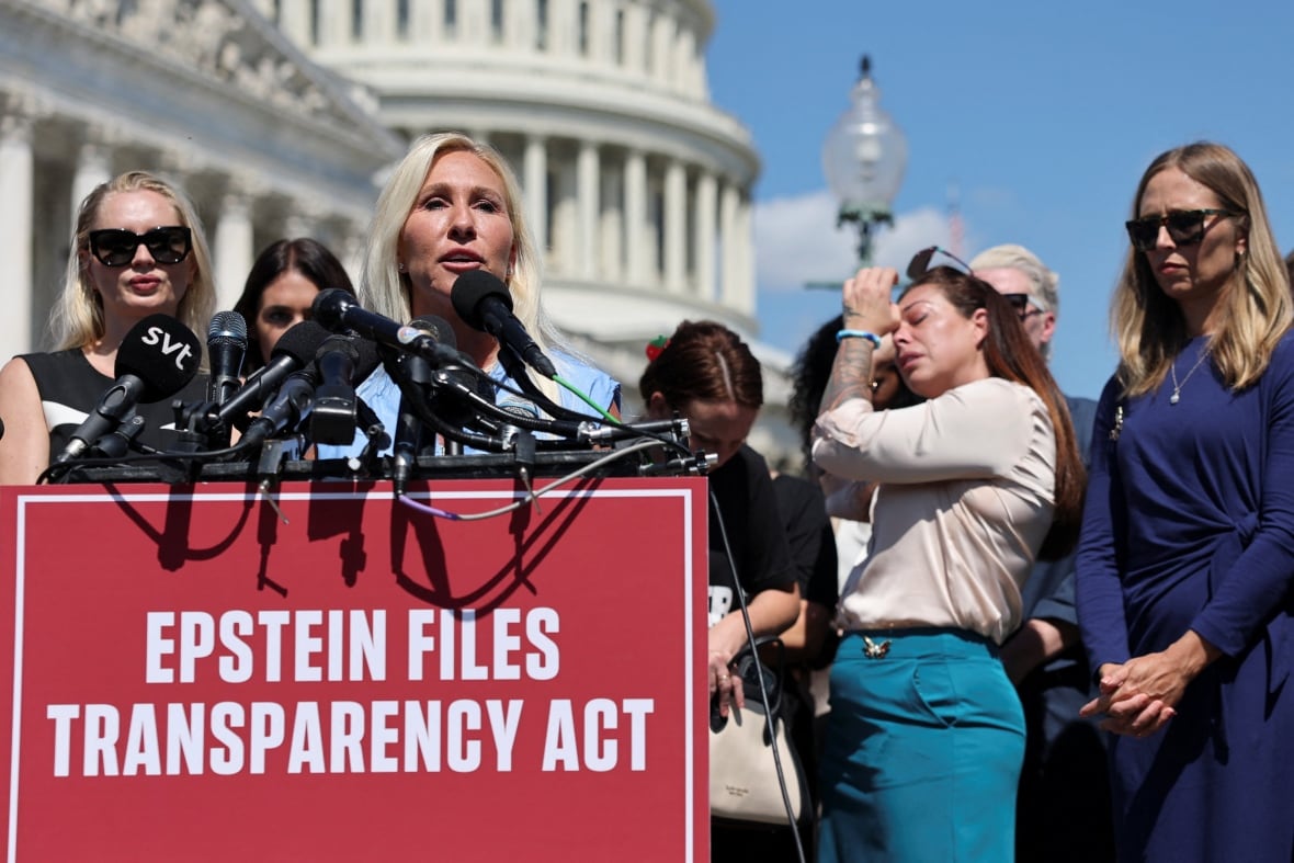 A politician wearing blue stands at a podium while a woman behind her wipes her eyes.
