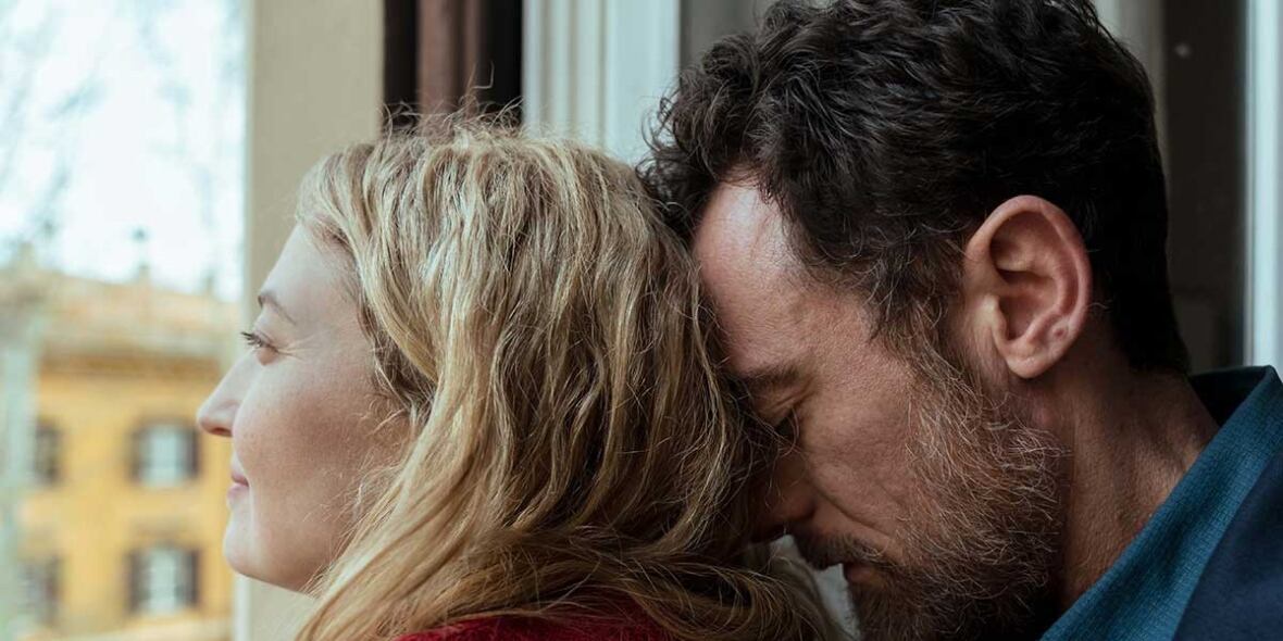 A white man and woman embrace by a window.