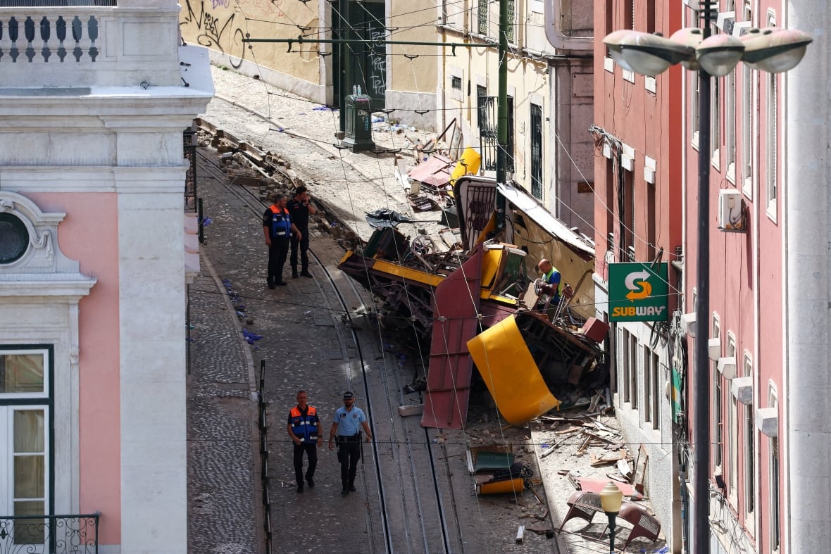 A yellow train car in a tight street, sharp, paved with gravel.