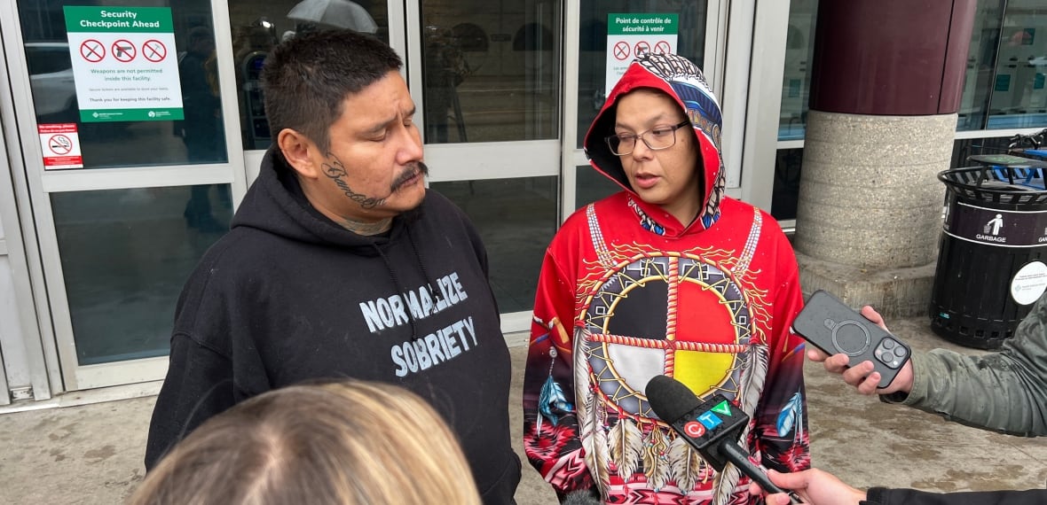 A man and a woman are in front of a group of reporters and microphones all standing in front of a hospital. 