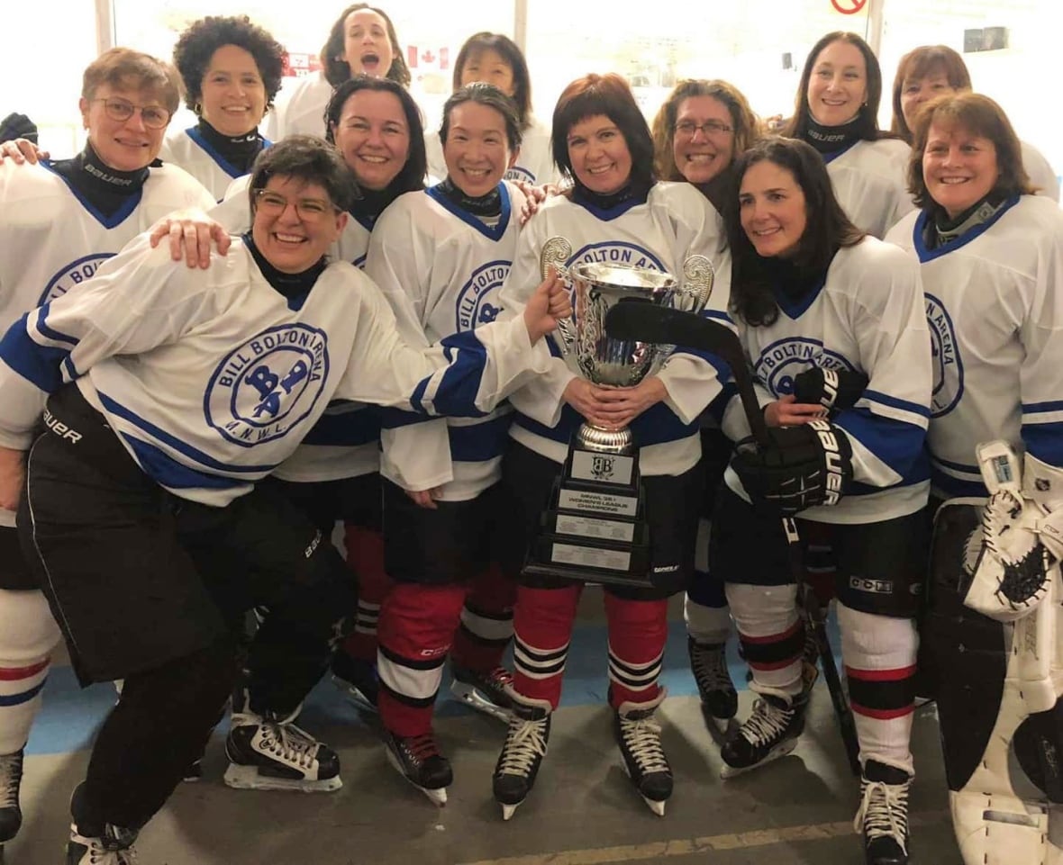 Frauen in Hockeyausrüstung lächeln in die Kamera und halten dabei eine silberne Trophäe.