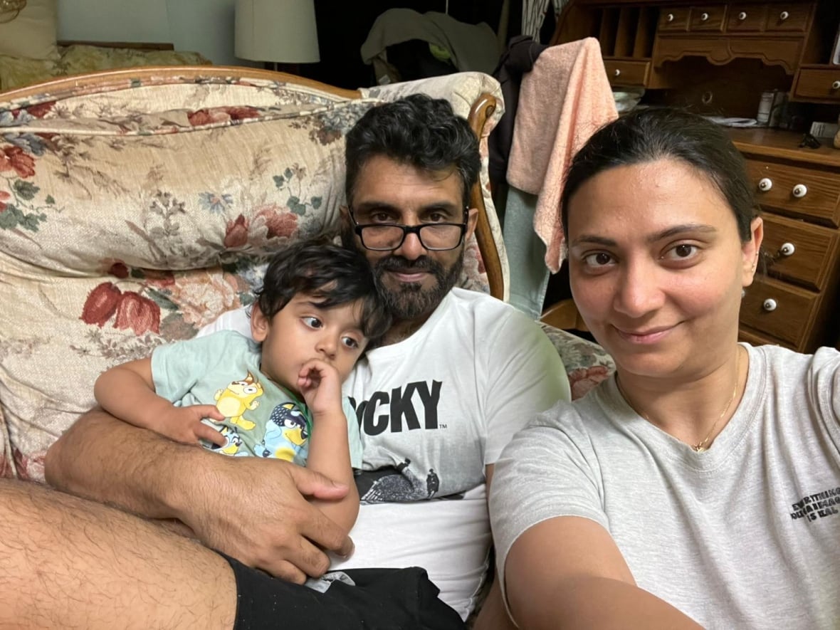 A woman, a man and a young child is seen in a personal photo, sitting on the sofa.
