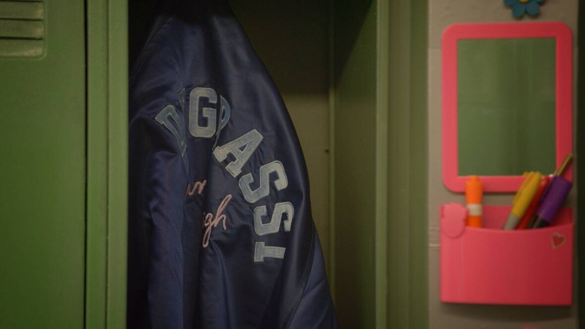 Close-up of a blue varsity jacket hanging in a green locker. 