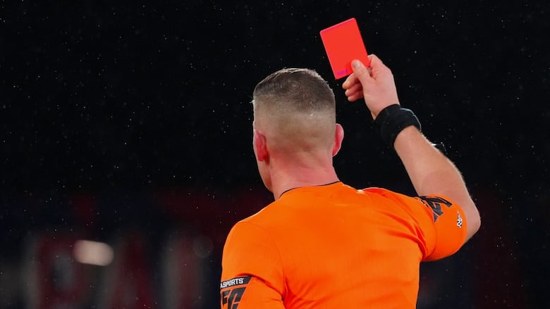 A photo of a referee holding up a red card during a December 2024 soccer game in London, England.