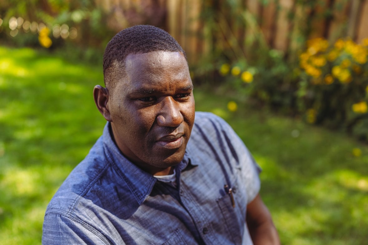 A black man wears a blue button sitting in the backyard.