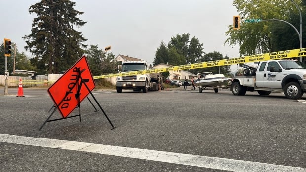 A detour sign on a road where a tow truck is lifting a pickup and a boat.