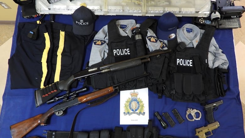 A table with shotguns, a belt, handcuffs, lights, RCMP uniforms and a light bar. 