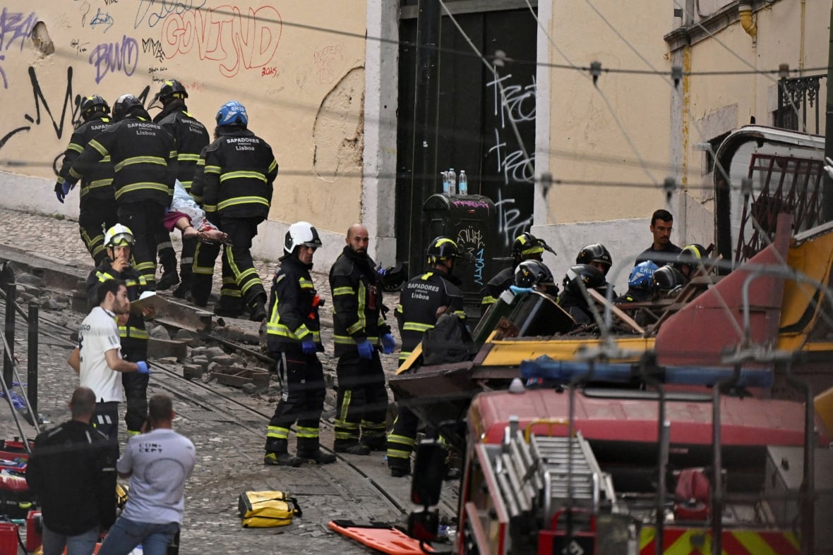 First responders removing a body on a stretcher away from a streetcar derailment on a narrow cobblestone street.