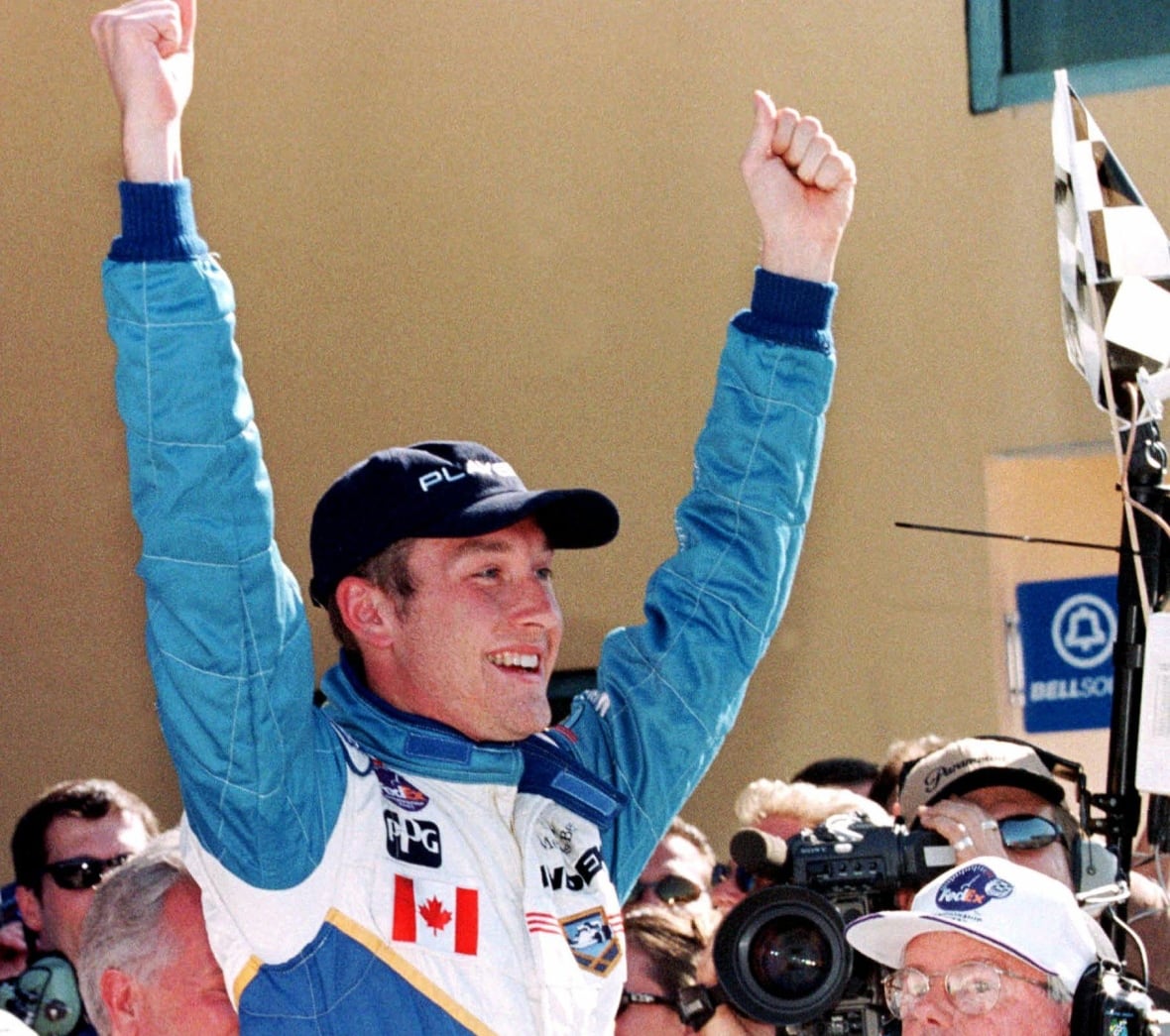 A young race car driver dressed in blue and white raises his arms in victory. 