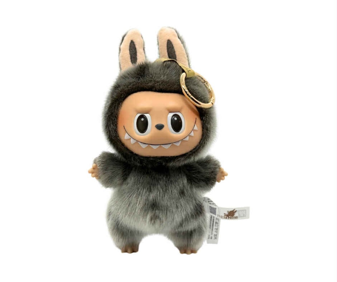 A little toy monster with against a white backdrop. It has a plastic face with big eyes and a pointy-toothed grin, while its body, head and rabbit-like ears are covered in a rich brown fur.