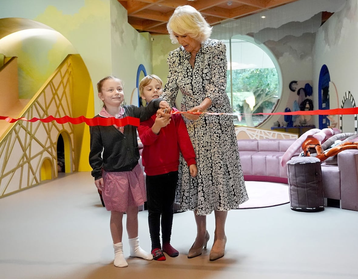 An adult and two child cut a red ribbon in a playroom.