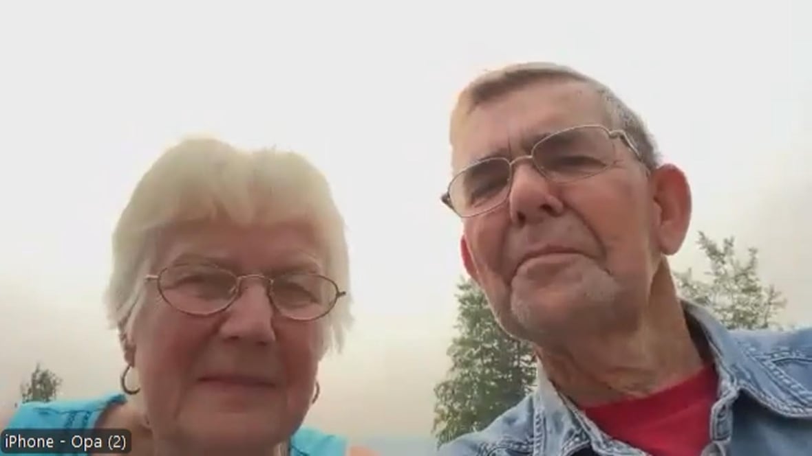 A man and woman speak to a camera with smoky skies behind them