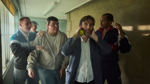 A man covers his ears as a group of teenage boys speak excitedly to him.
