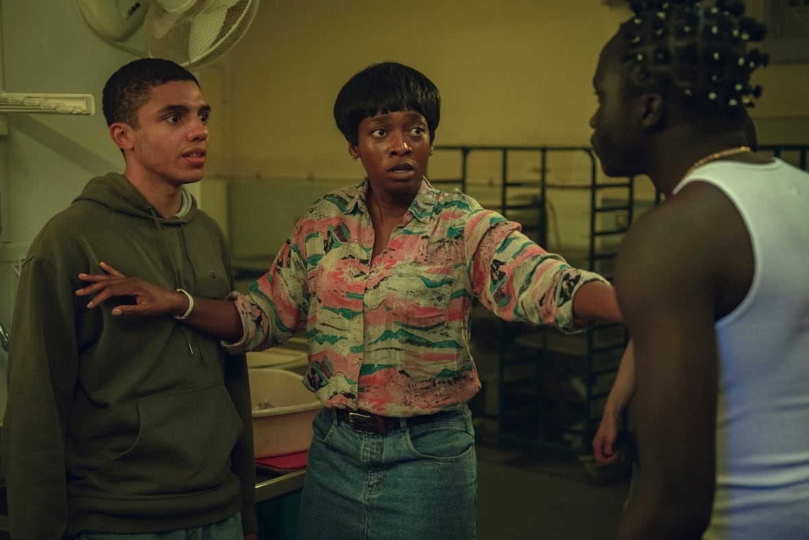 Two teenager boys stand separate by a woman with her arms on each of their chests.