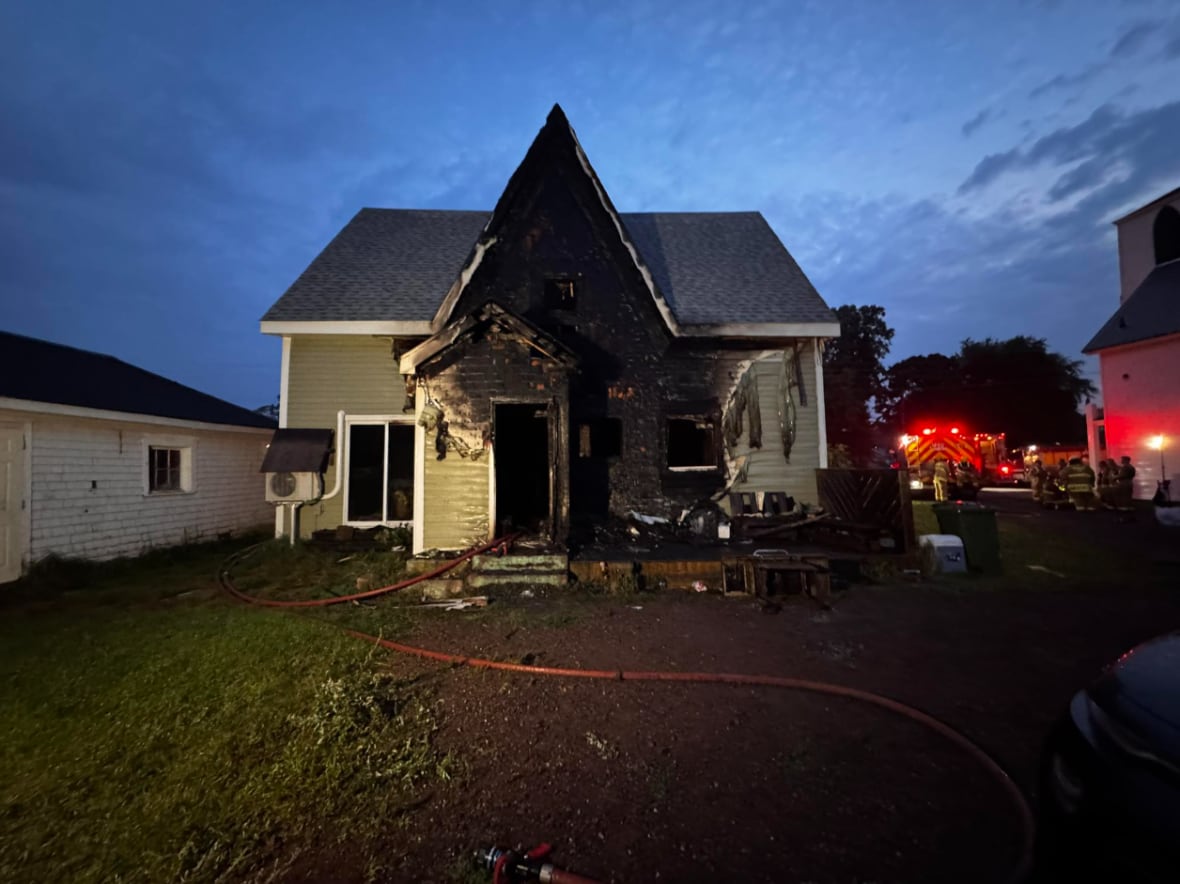 A burned home with emergency lights to the right of the house.