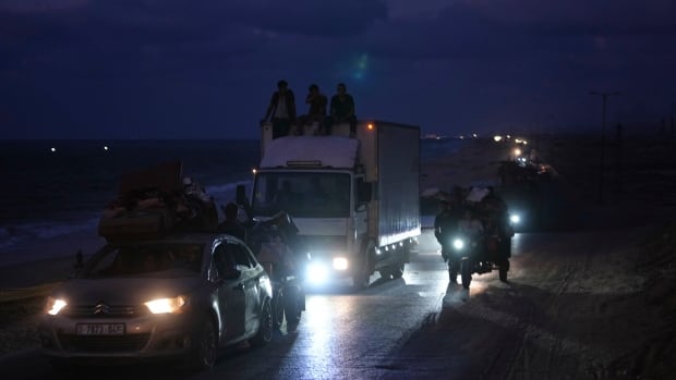 Displaced Palestinians fleeing northern Gaza carry their belongings along the coastal road toward southern Gaza, Saturday, Sept. 6, 2025. A convoy of cars and trucks is seen travelling alongside a beach at night.