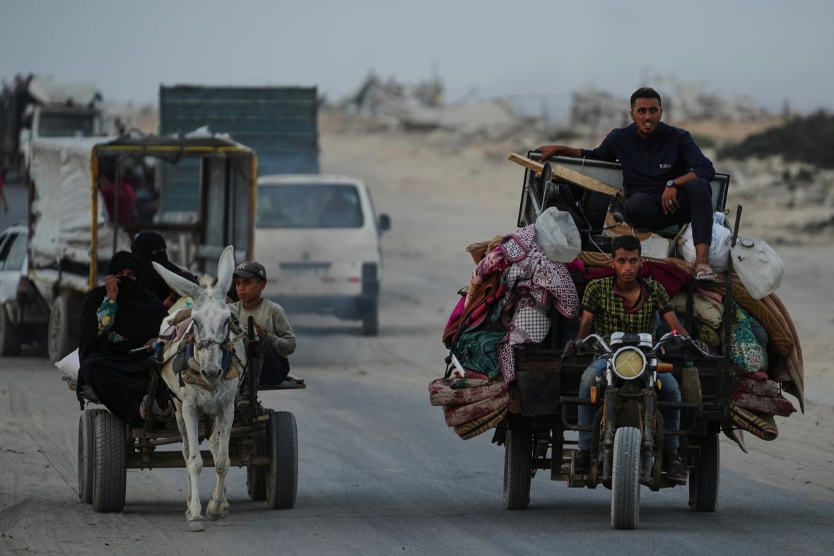 We see people traveling on a motorcycle and donkey on a dusty road.
