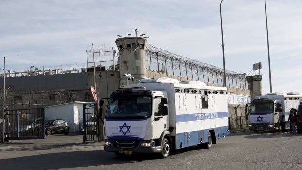 Military buses drive past the exterior of a prison.