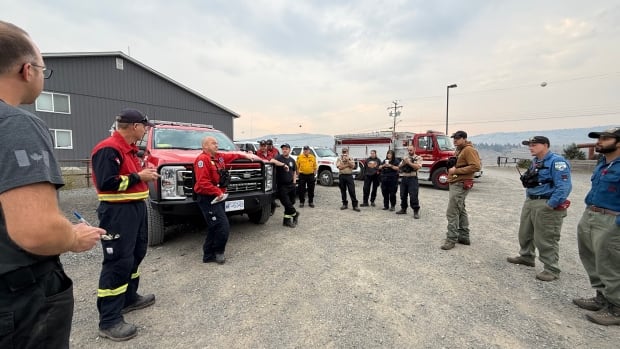 A group of men are seen talking near fire trucks.