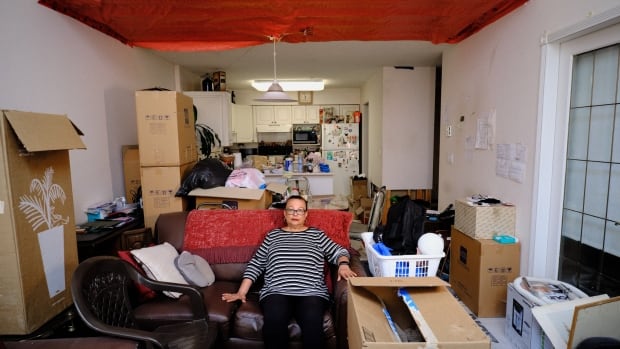 A woman sits on a couch in an apartment with the ceiling covered in an orange tarp.