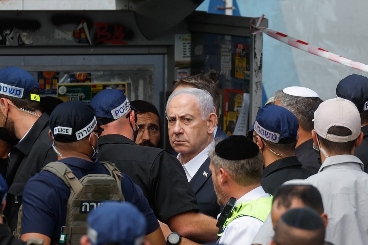 Many people are displayed in the open air. A man with a prominent white hair, surrounded by police officers with military uniforms.