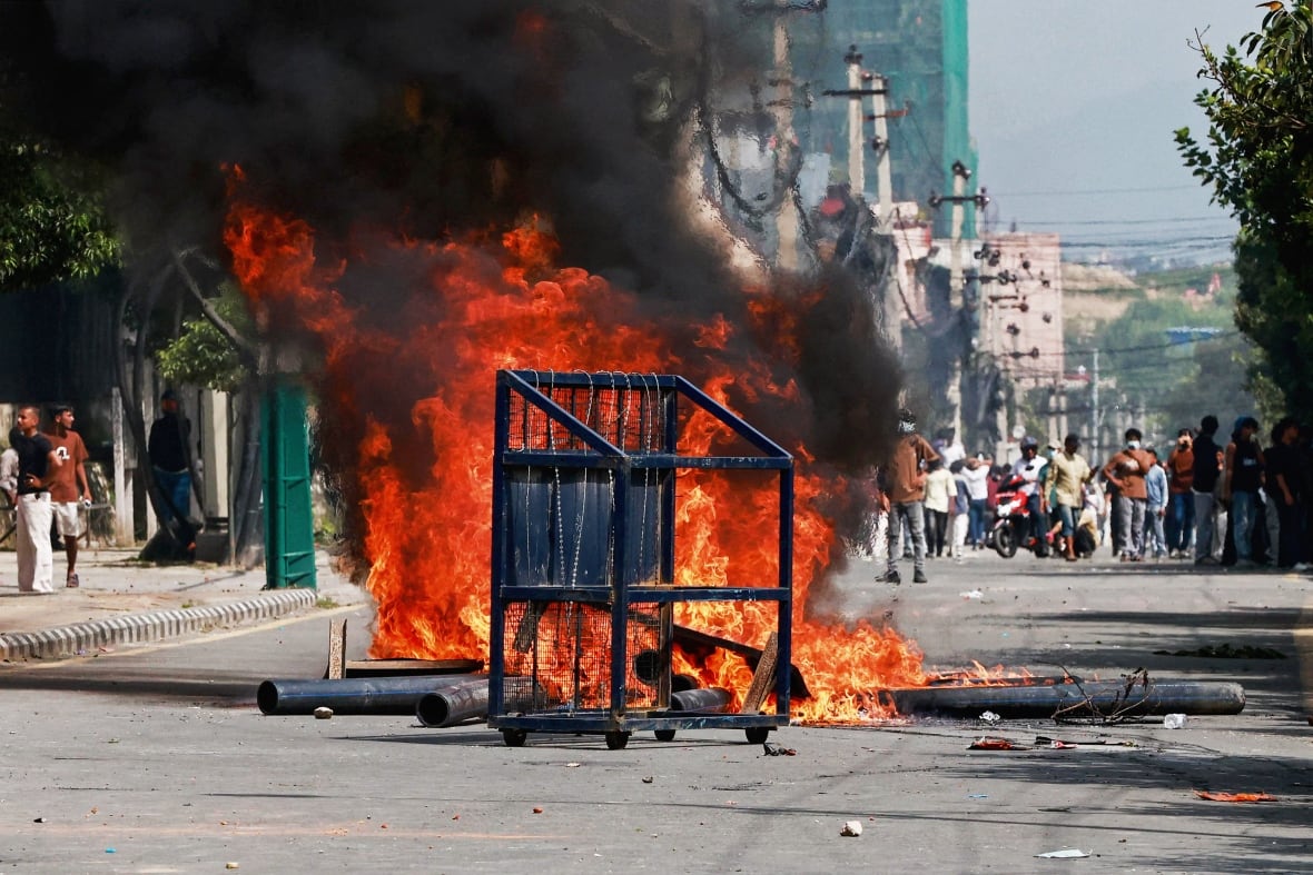 A structure is on fire, with large orange flames in the middle of a street.