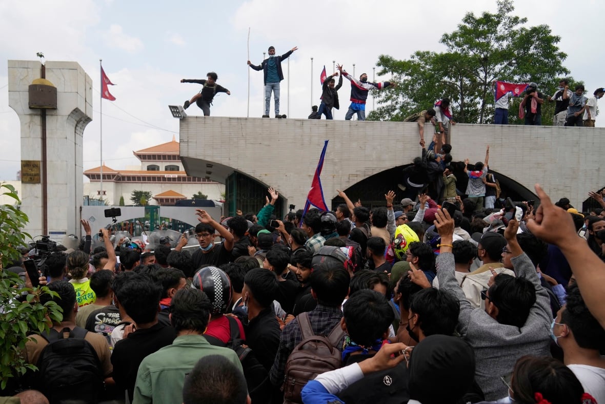 Dozens of people are shown in a crowd in an apparent demonstration, other people standing above a building above.