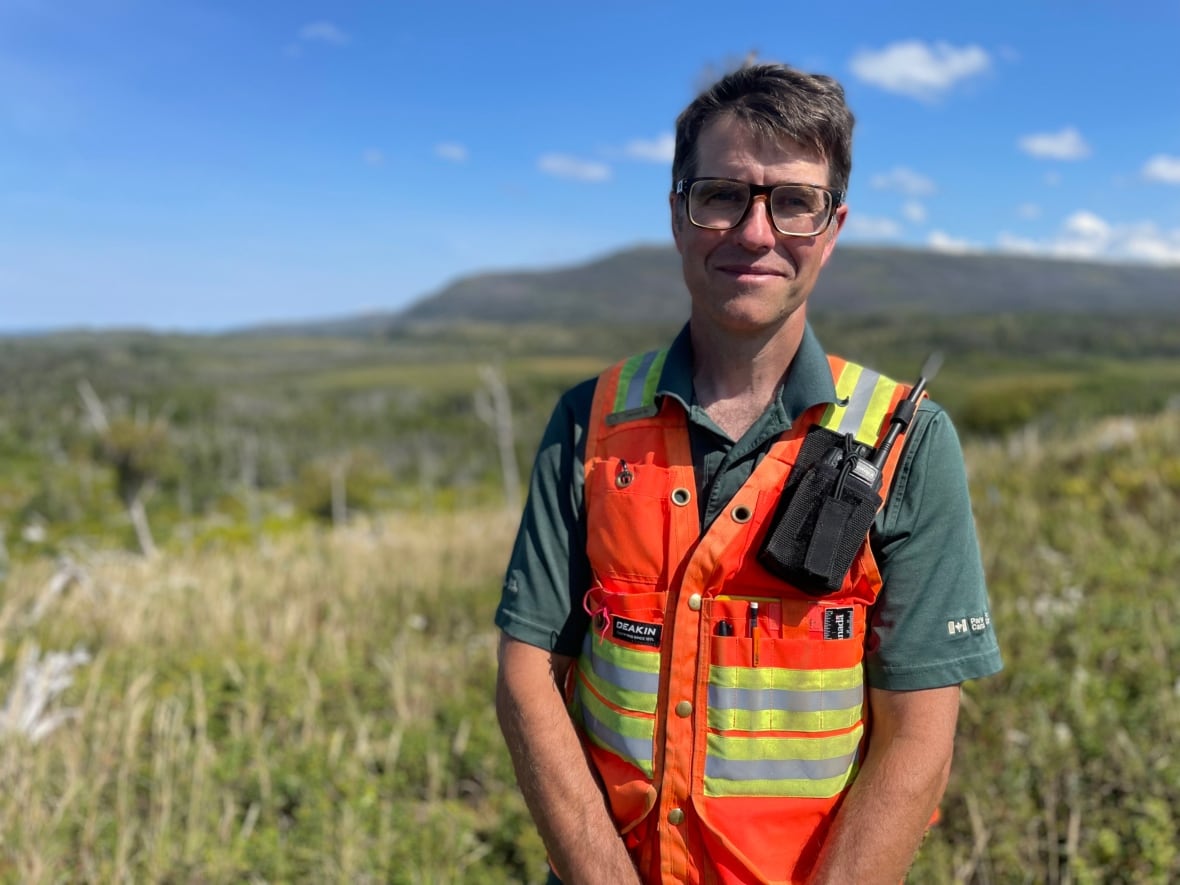 A man in a safety vest standing on top of a mountain.