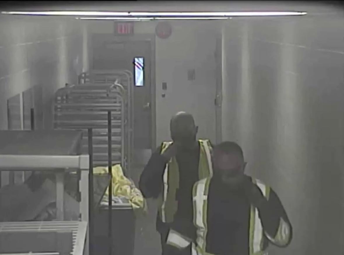 Men wearing high-vis vests walk through a corridor.