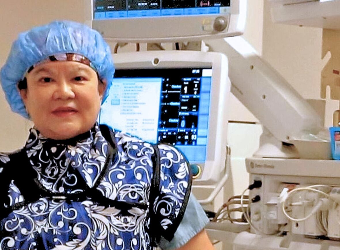 Woman wearing medical hair net and scrubs in front of monitors. 