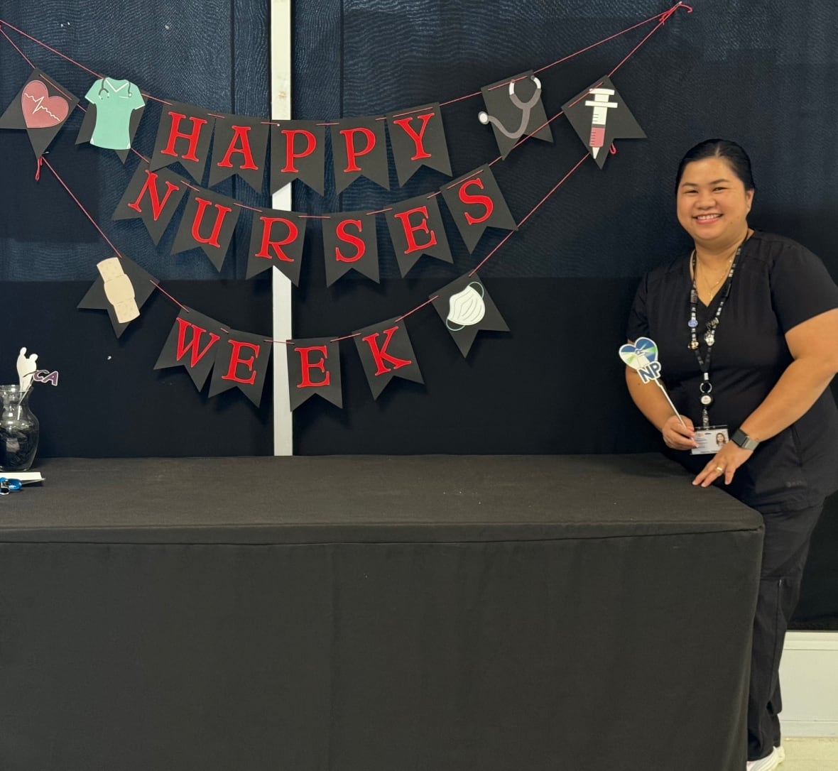 Nurse in scrubs standing next to sign that says happy nurses week.