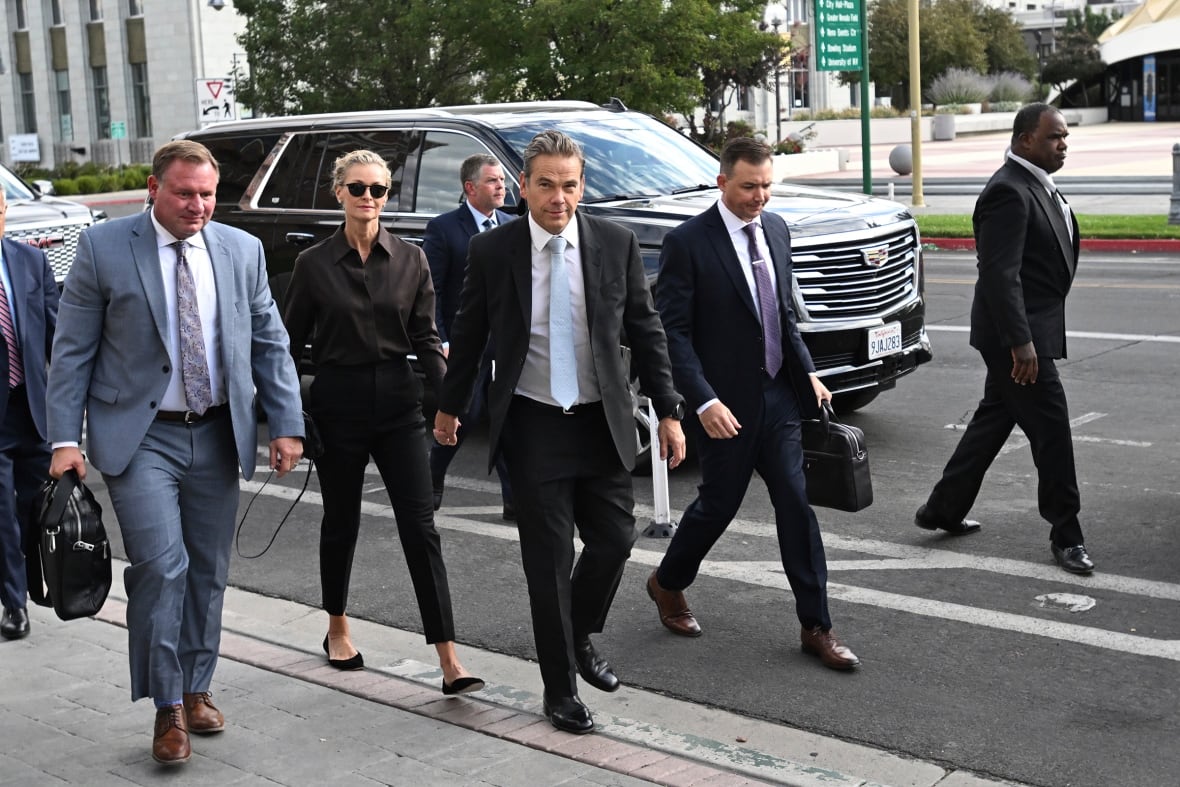 A group of men in suits, along with one woman in a suit, walk along a sidewalk