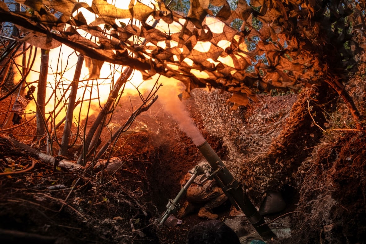 A closeup of a trench in a forested area is shown, with smoke pouring out of a weapon firing ammunition from the bunker.