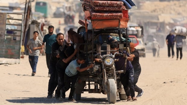 Men and boys push along their belongings, all piled on top of one another on a vehicle.