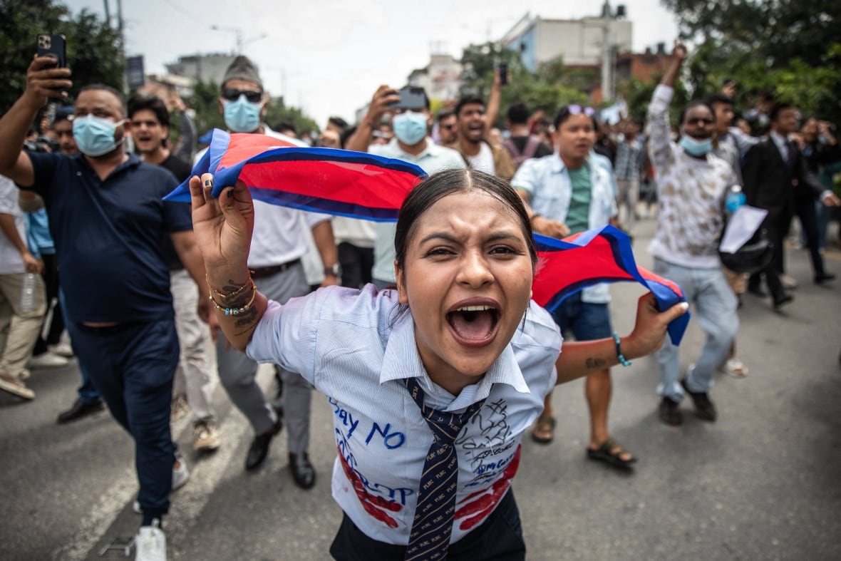 A young woman is closer to the camera wearing a shirt and tie a tie while holding a flag, as some follow after a visible road post.