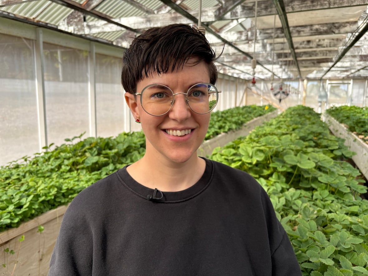 A woman stands in a screenhouse with plants visible behind her.